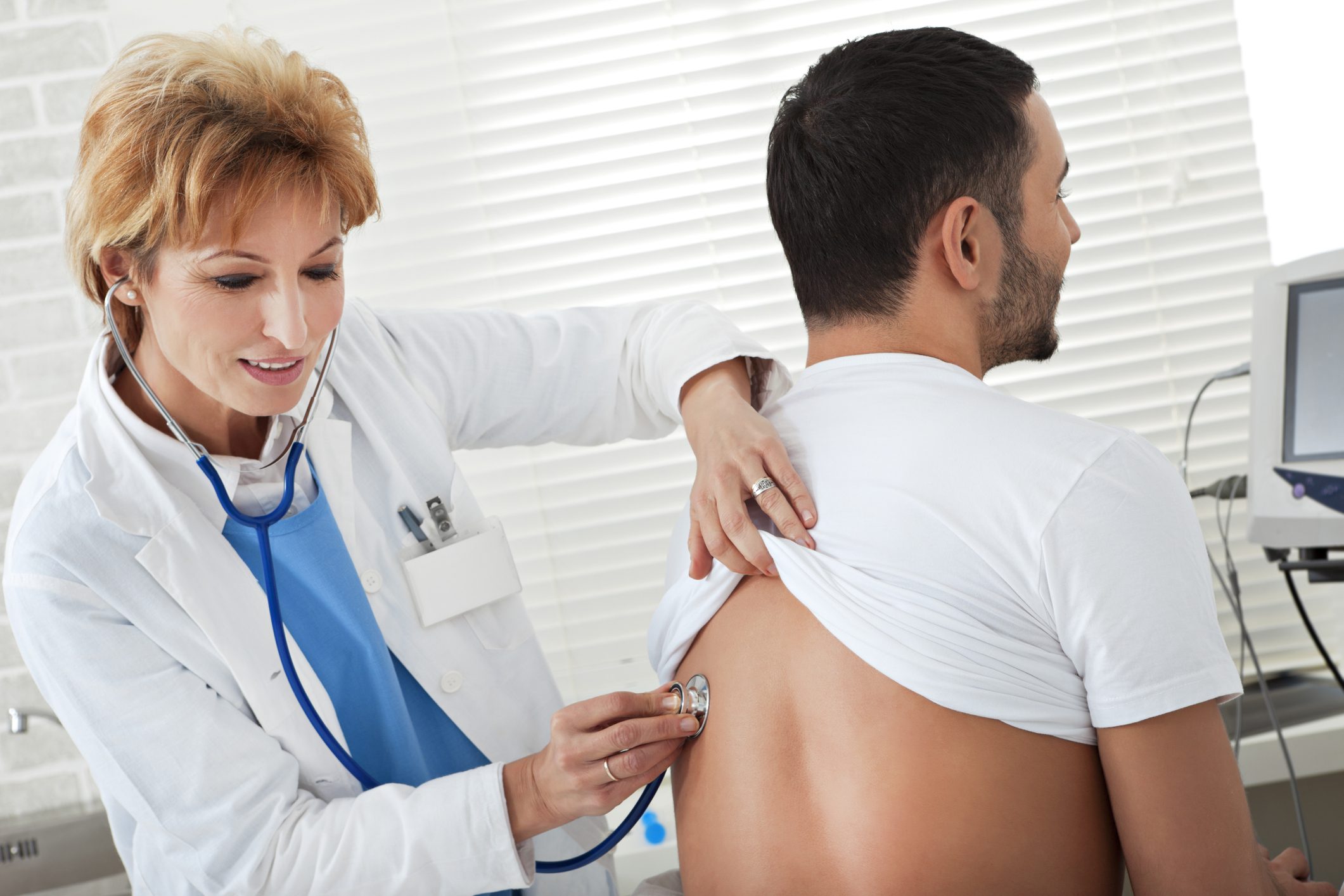 Doctor examining patient's back with stethoscope.